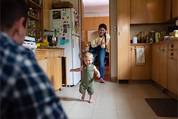 Toddler learning to walk with parents in kitchen. Toddler learning to walk with parents in kitchen.
